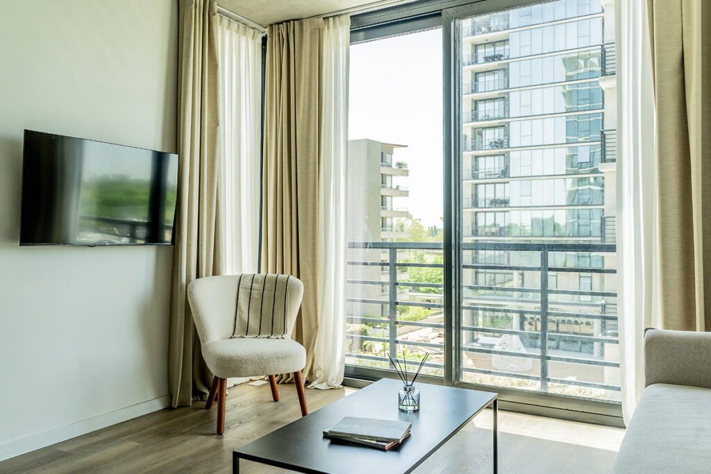 Rincón de descanso con sillón de diseño, Smart TV de pared y ventanal con vista a la arquitectura exterior.