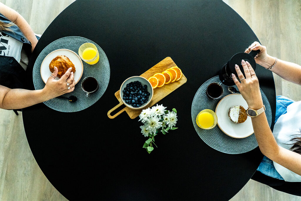 Vista superior del desayuno para dos con café, jugo de naranja, arándanos y frutas en una mesa redonda negra.