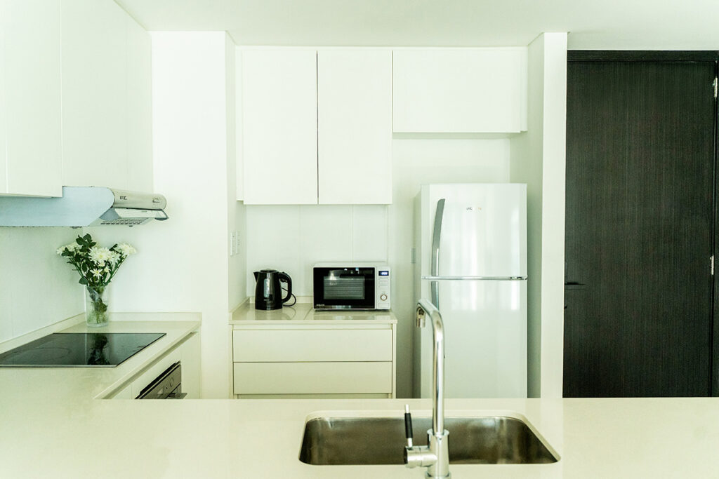 Cocina integrada con heladera, microondas, pava eléctrica y grifería moderna, lista para su uso.