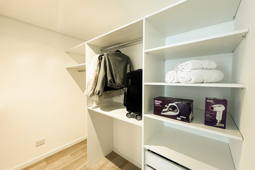 Vestidor con plancha, secador de pelo en cajas y toallas blancas limpias apiladas en los estantes.