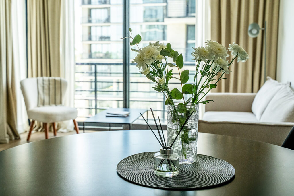 Flores frescas y difusor de aromas sobre la mesa de comedor, con el living y ventanal desenfocados al fondo.