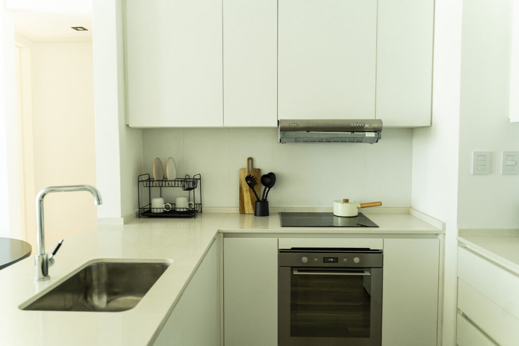 Cocina moderna en blanco con horno empotrado, anafe de inducción y campana extractora.