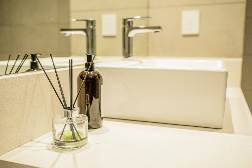 Detalle del lavamanos del baño con grifería moderna, bacha de porcelana blanca y un difusor de aromas.